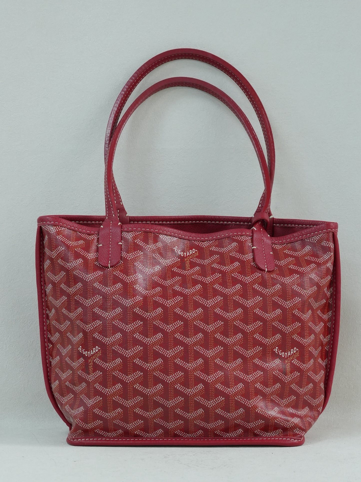 Front view of red Goyardine chevron canvas mini reversible tote with calfskin trim and dual top handles.