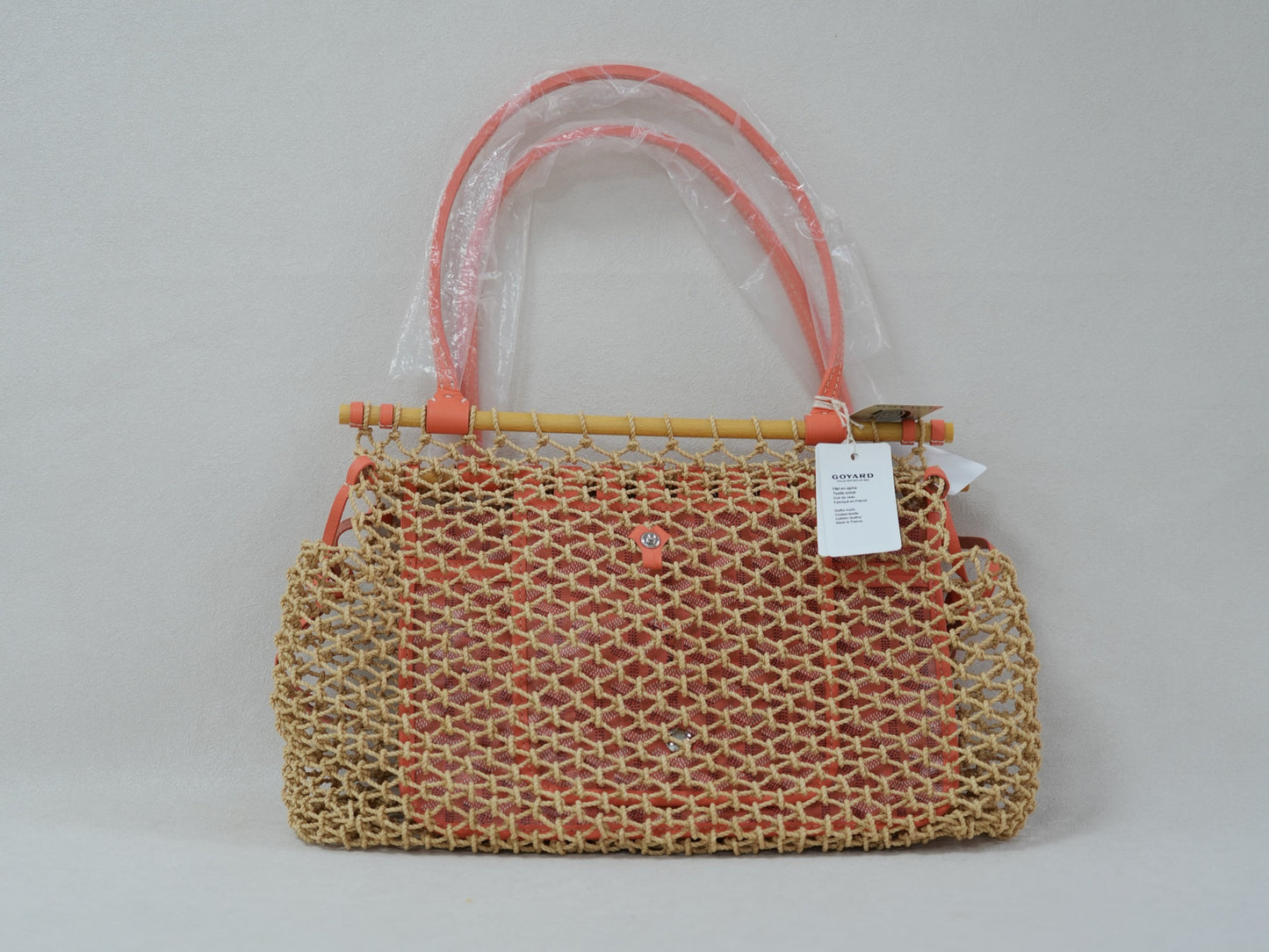 Front view of coral woven net tote with beech wood top bar, leather trim and removable Goyardine canvas inner pouch.