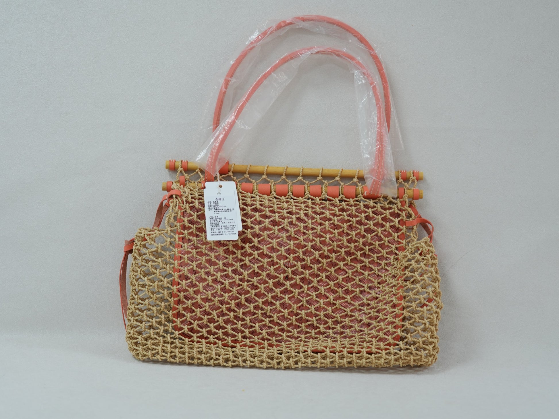 Back view of coral woven net tote with beech wood top bar, leather trim and removable Goyardine canvas inner pouch.